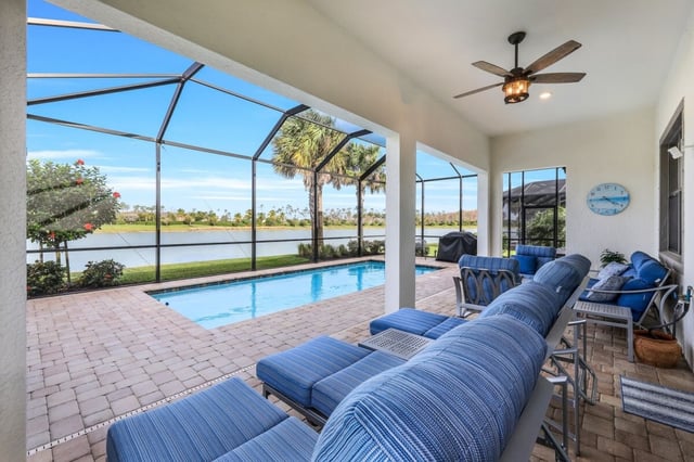Screened lanai with blue cushioned loungers, a ceiling fan and a pool overlooking a lake and palm trees