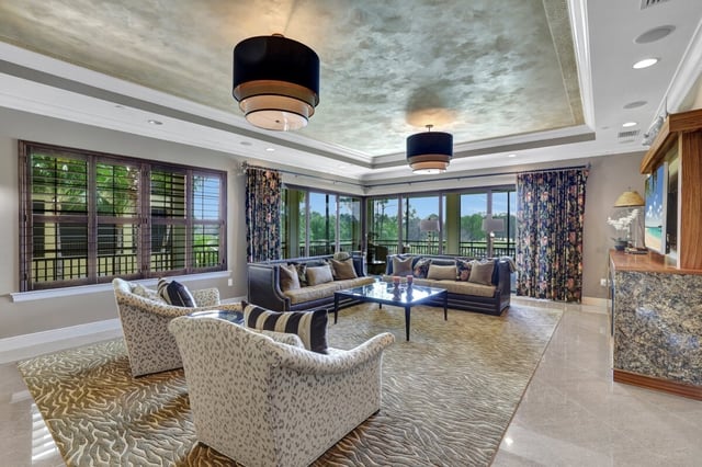 Spacious living room with tray ceiling, drum pendant lights, patterned armchairs and large windows overlooking greenery