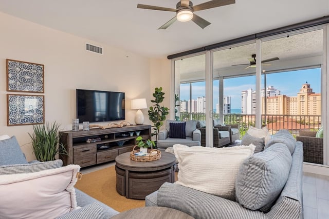 Bright condo living room with striped sofas, ceiling fan and floor-to-ceiling windows framing a resort and Gulf view