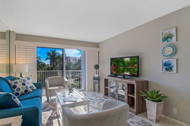 Bright condo living room with teal sofa, flat-screen TV and balcony doors framing palm trees