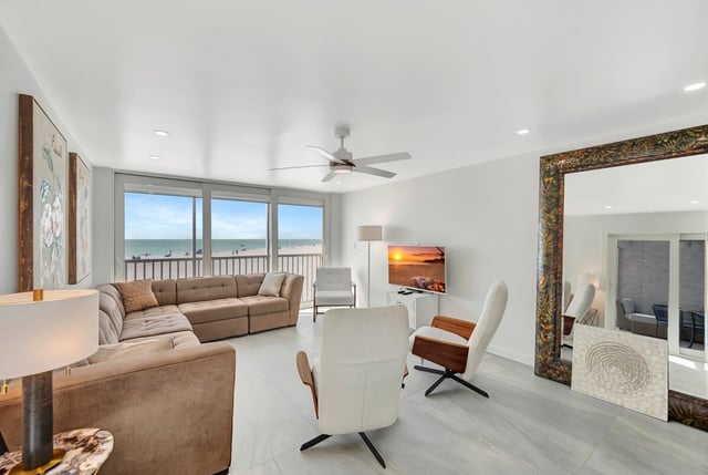 Bright beachfront condo living room with sectional sofa, ceiling fan and sliding doors framing a Gulf view