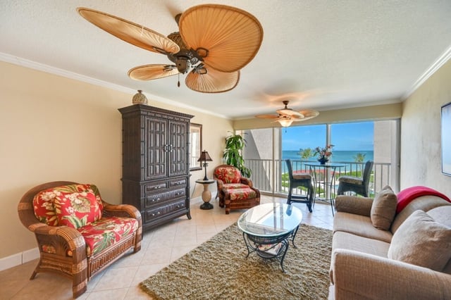 Condo living room with palm-leaf ceiling fans, tropical print chairs and a balcony overlooking the Gulf