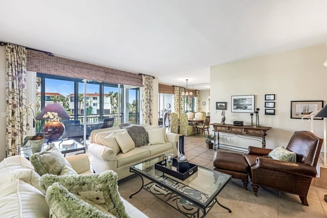 Condo living room with cream sofas, leather armchairs and glass coffee table facing a sunlit balcony