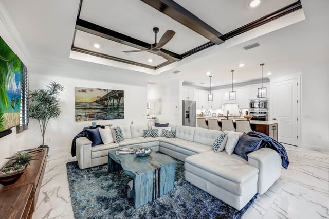 Open-plan living room with white sectional sofa, blue rug, coffered ceiling and kitchen with breakfast bar beyond