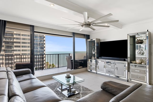 Condo living room with leather sectional, mirrored cabinets and ceiling fan opening to a balcony with Gulf views
