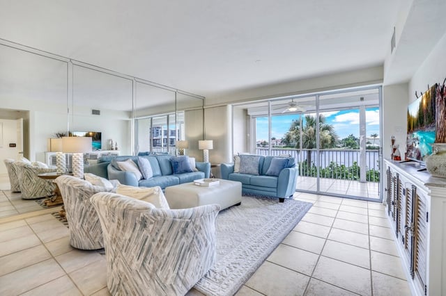 Bright coastal condo living room with blue sofas, mirrored wall and sliding doors opening to a waterfront balcony