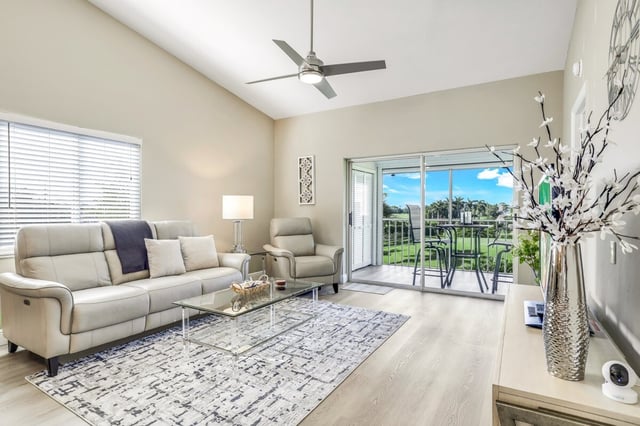 Bright condo living room with cream sofa, ceiling fan and sliding doors opening to a screened lanai with golf course views