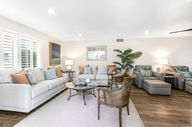 Bright coastal living room with white sofas, blue and coral pillows, palm plant and plantation shutters