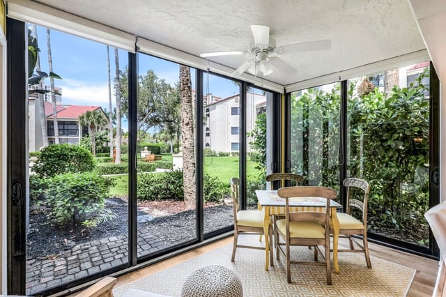 Bright screened lanai with ceiling fan, wicker dining set and floor-to-ceiling glass overlooking palms and green lawn
<br>