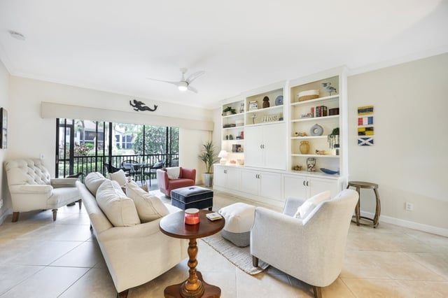 Bright living room with cream sofas, built-in white shelving, tile floors and sliding doors to a screened lanai
