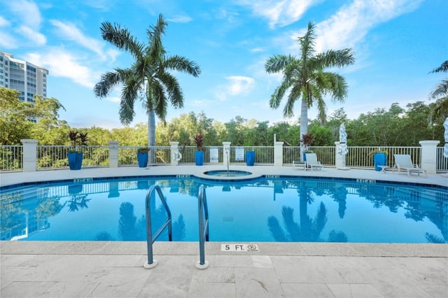 Resort-style swimming pool with attached hot tub, royal palms, blue planters and white railings under a bright sky