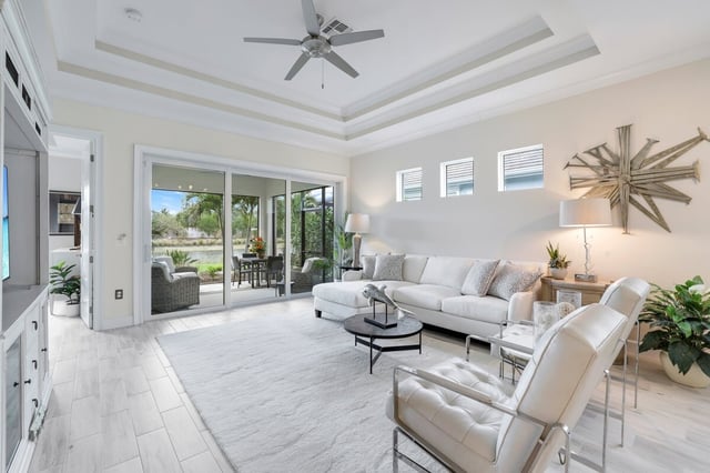 Bright white living room with tray ceiling, ceiling fan, tufted armchairs and sliding doors to a screened lanai
