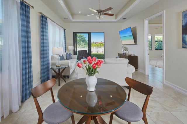Bright vacation rental living room with glass dining table, pink tulips, white sofas and blue patterned curtains