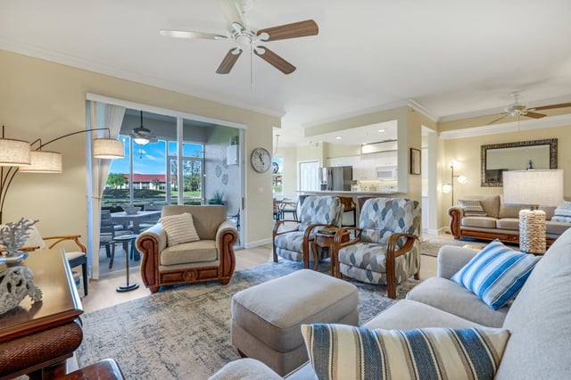Bright open-plan condo living room with ceiling fan, patterned armchairs and sliding doors to a screened lanai