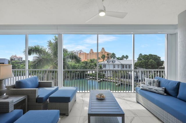 Screened balcony with blue cushioned wicker furniture overlooking a waterway, palm trees and resort buildings
