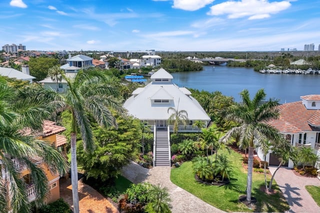Aerial view of a white metal-roof stilt home surrounded by palms along a calm waterway with boat docks
Answer in no more than 500 words