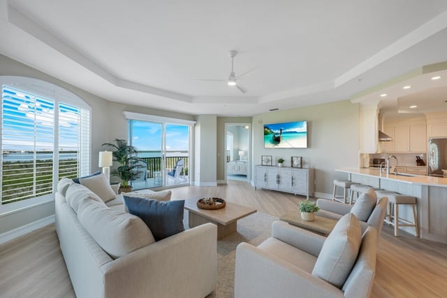 Bright coastal condo living room with white sofas, ceiling fan, and arched window overlooking the water