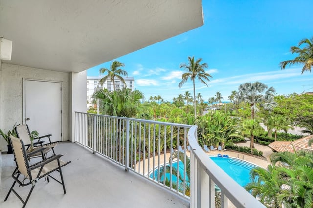 Condo balcony with folding chairs overlooking a palm-lined pool and blue sky