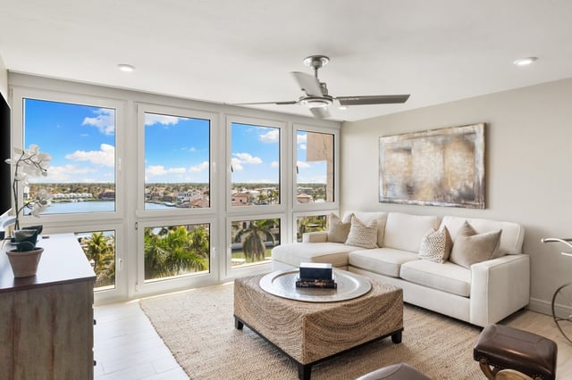 Bright condo living room with cream sectional, woven coffee table and floor-to-ceiling windows framing a waterway view