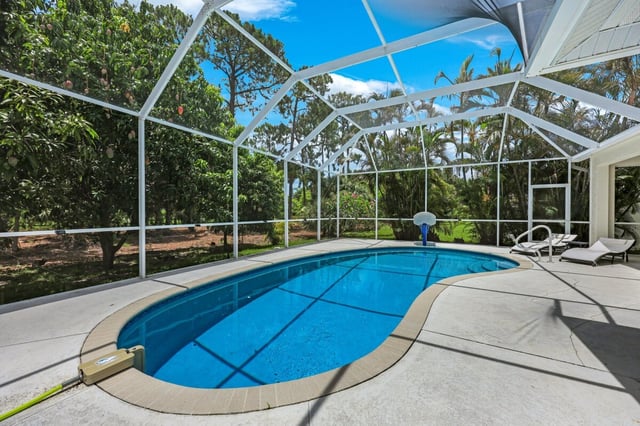 Screened-in kidney-shaped pool with lounge chairs on a sunny patio surrounded by lush tropical trees
```