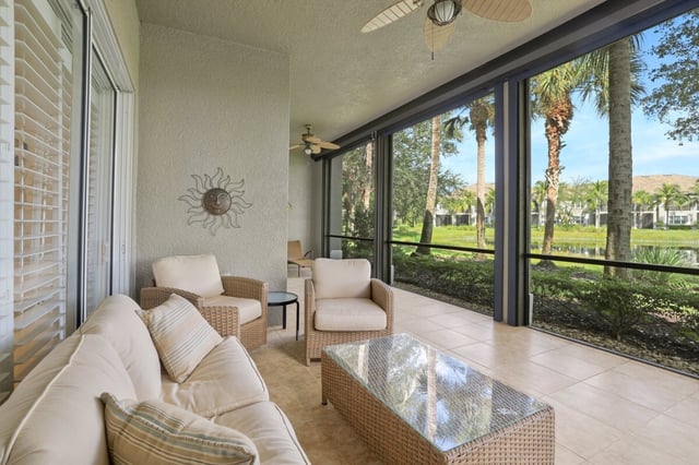 Screened lanai with wicker seating, ceiling fans and a sun wall art piece overlooking palm trees and a lake
```