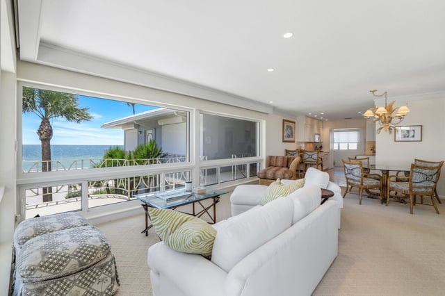 Bright condo living room with white sofa, glass coffee table and picture window framing palm trees and the Gulf