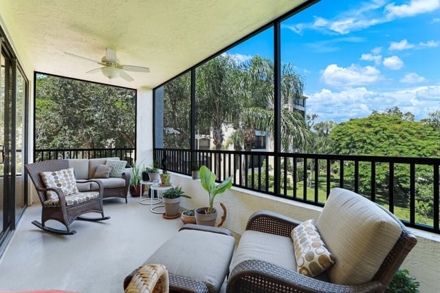 Screened lanai with wicker seating, ceiling fan and potted plants overlooking palms and blue sky