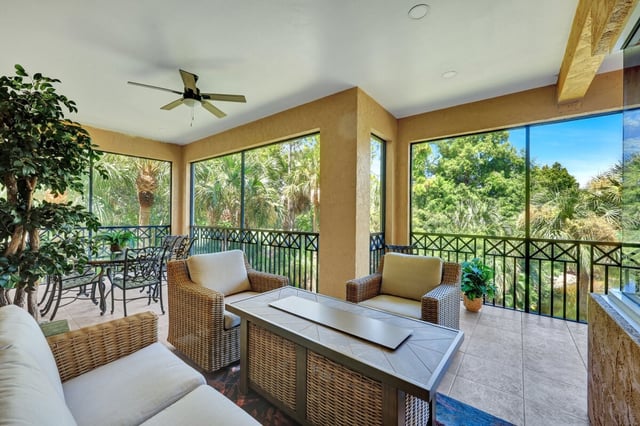 Screened lanai with wicker seating, ceiling fan and dining table overlooking palms and lush greenery
