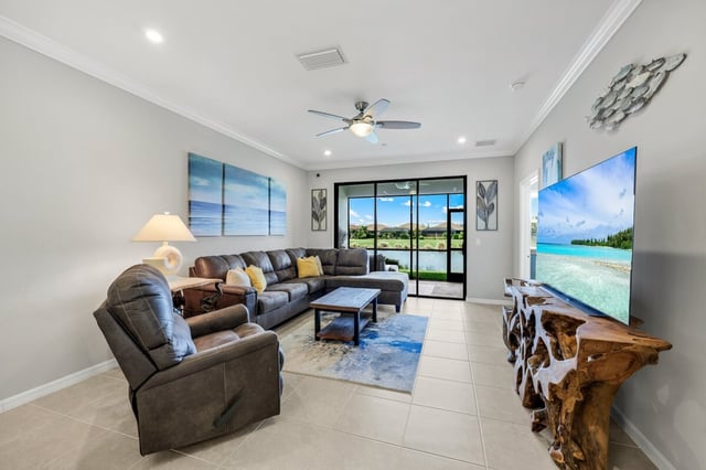 Bright living room with gray sectional, ceiling fan, driftwood TV stand, and sliding doors to a golf course view