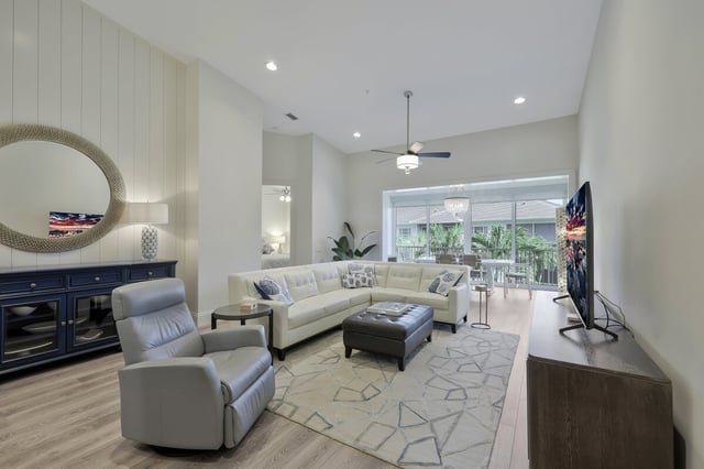 Bright living room with white sectional sofa, gray recliner, patterned rug and sliding doors to a screened lanai