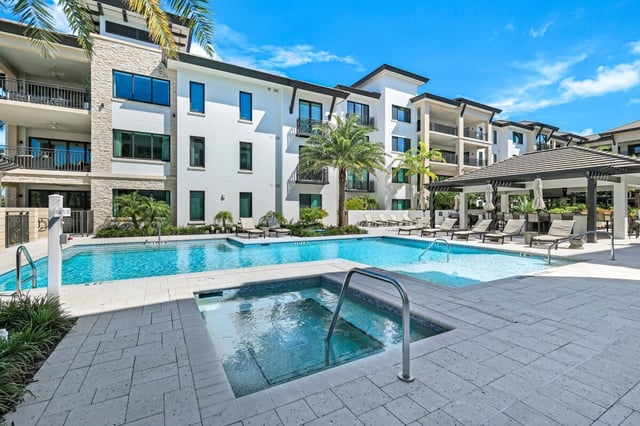 Resort-style pool and spa with lounge chairs, palms and a shaded cabana beside a white condo building