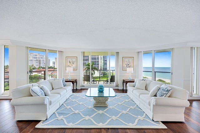 Bright condo living room with two white sofas facing a glass coffee table and windows overlooking the Gulf