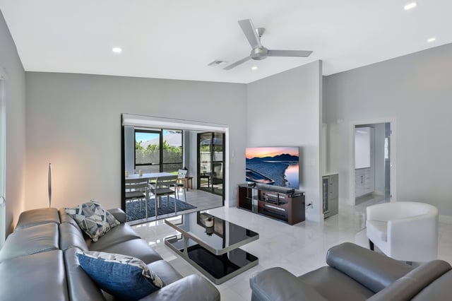 Bright living room with gray leather sectional, ceiling fan, flat-screen TV and sliding doors to a patio