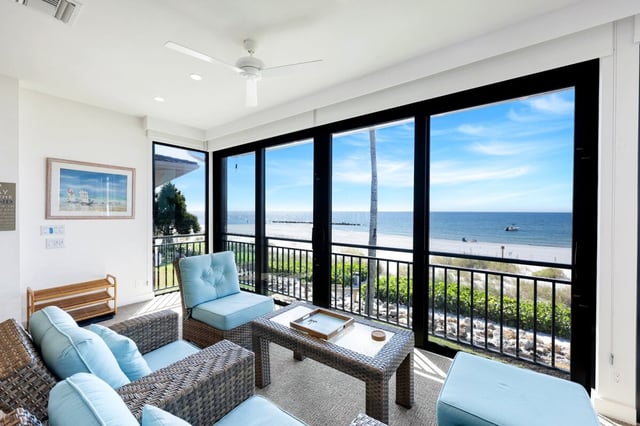 Screened lanai with wicker furniture and blue cushions overlooking the beach and Gulf waters