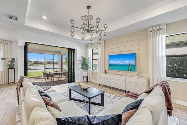 Bright open living room with cream sectional sofa, sputnik chandelier, wall-mounted TV and sliding doors to a lakefront lanai