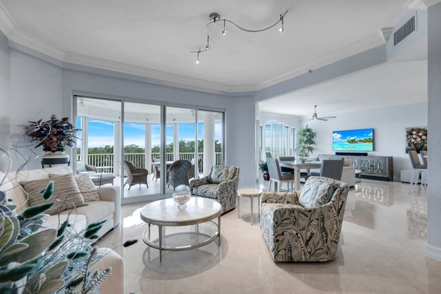 Bright condo living room with patterned armchairs, marble floors and sliding glass doors opening to a balcony view
