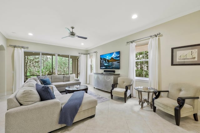 Bright living room with a sectional sofa, armchairs, wall-mounted TV, ceiling fan and tile floors
