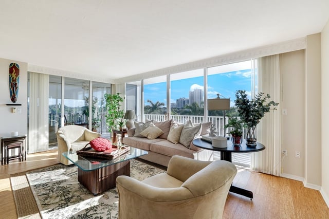Bright condo living room with floor-to-ceiling windows framing blue sky, palms and high-rise views