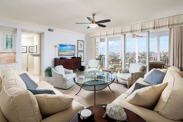 Bright condo living room with cream sofas, glass coffee table, ceiling fan and balcony doors opening to a Gulf view