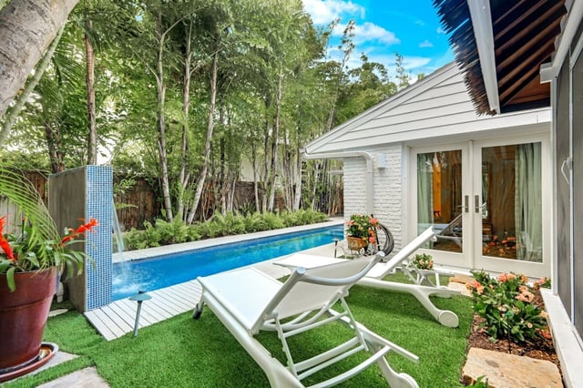 White lounge chairs on turf beside a narrow lap pool with blue tile water feature and cottage patio doors