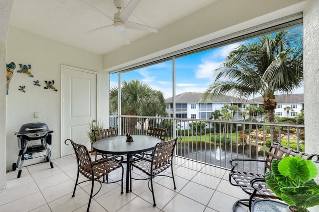 Screened lanai with patio table, chairs and grill overlooking palm trees, a pond and condo buildings