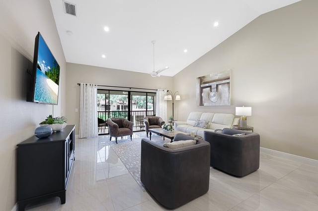 Bright vacation rental living room with vaulted ceiling, wall-mounted TV, cream sofa and sliding doors to a screened lanai