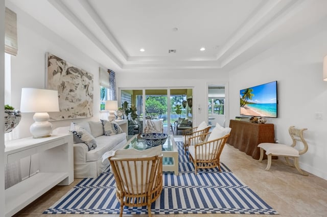 Bright coastal living room with white sofa, striped blue rug, rattan chairs and sliding doors to a patio