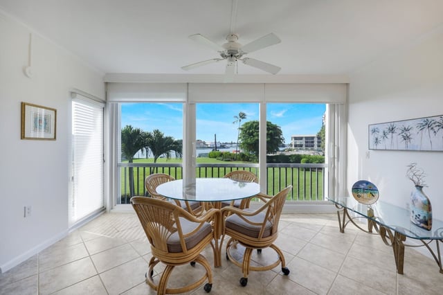 Bright dining nook with rattan chairs, glass table and ceiling fan overlooking a lawn and waterway through sliding glass doors