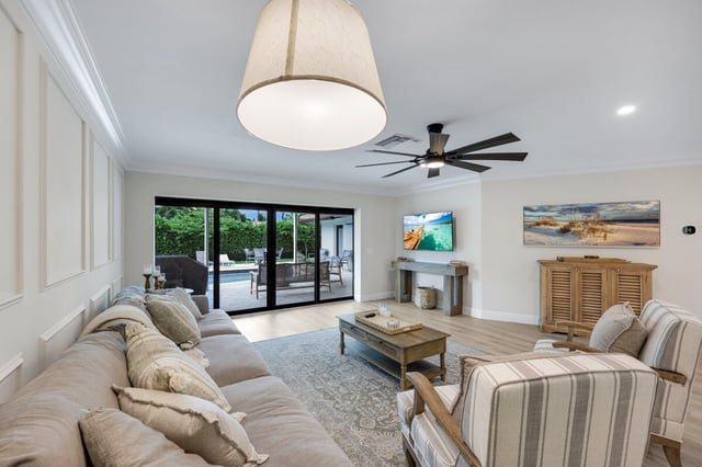 Bright coastal living room with sectional sofa, striped armchairs, drum pendant light and sliding glass doors to a pool patio