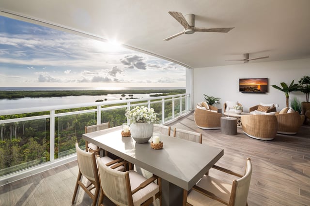 Covered condo terrace with dining table, wicker lounge chairs and ceiling fans overlooking mangroves and water at sunset