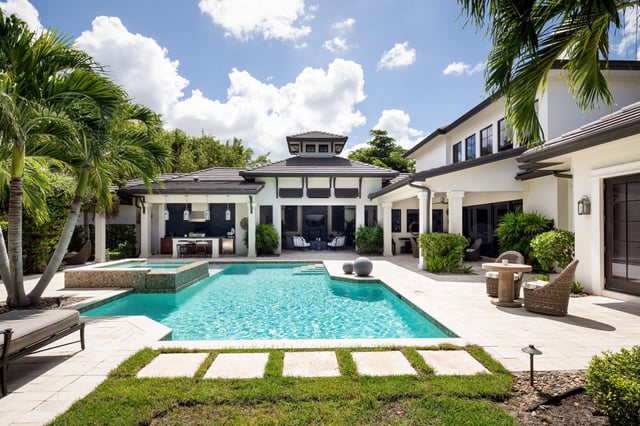 Turquoise pool and raised spa framed by palms and a covered lanai at a white luxury vacation home