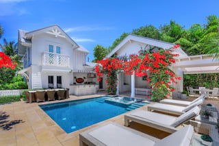 White coastal home with a turquoise pool, outdoor bar, lounge chairs and red bougainvillea in bloom