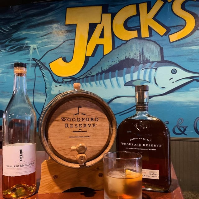 Bourbon bottle, small oak barrel and an old fashioned cocktail on a bar at Jack's, with a painted marlin mural behind