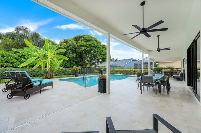 Covered lanai with ceiling fans and dining set overlooking a screened pool, loungers and tropical palms under blue sky